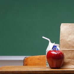 Brown bag lunch on a school desk in front of green chalkboard