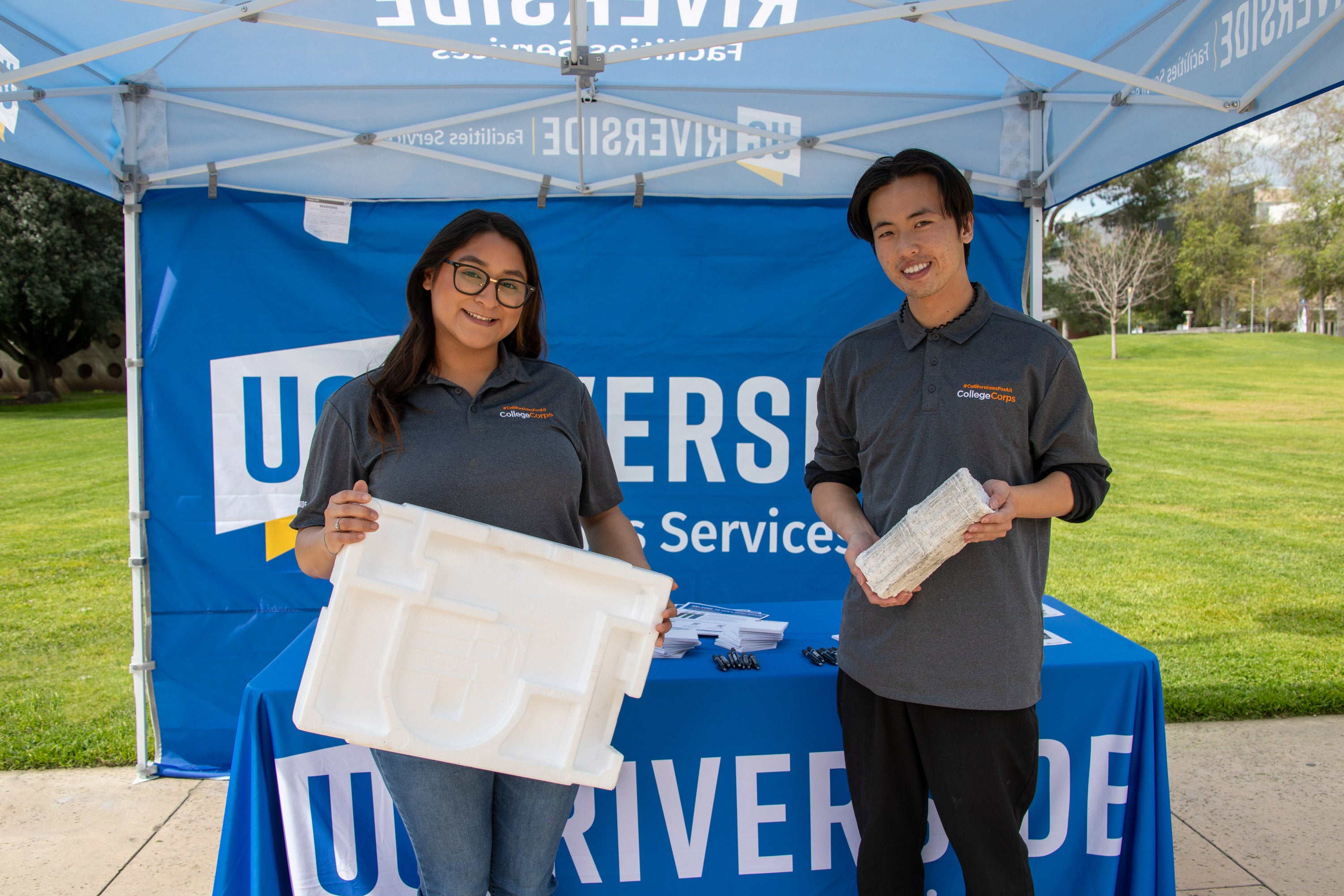 Two people at an event table holding Styrofoam meant for recycling