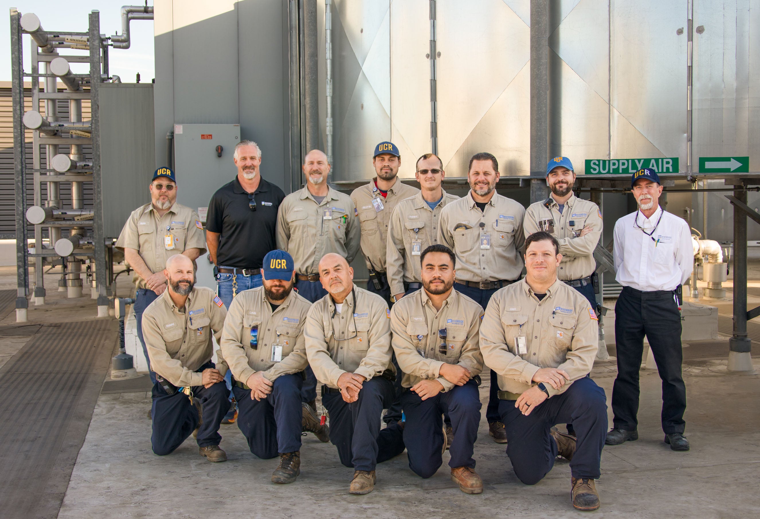 Team of building mechanical workers in front of air handler equipment
