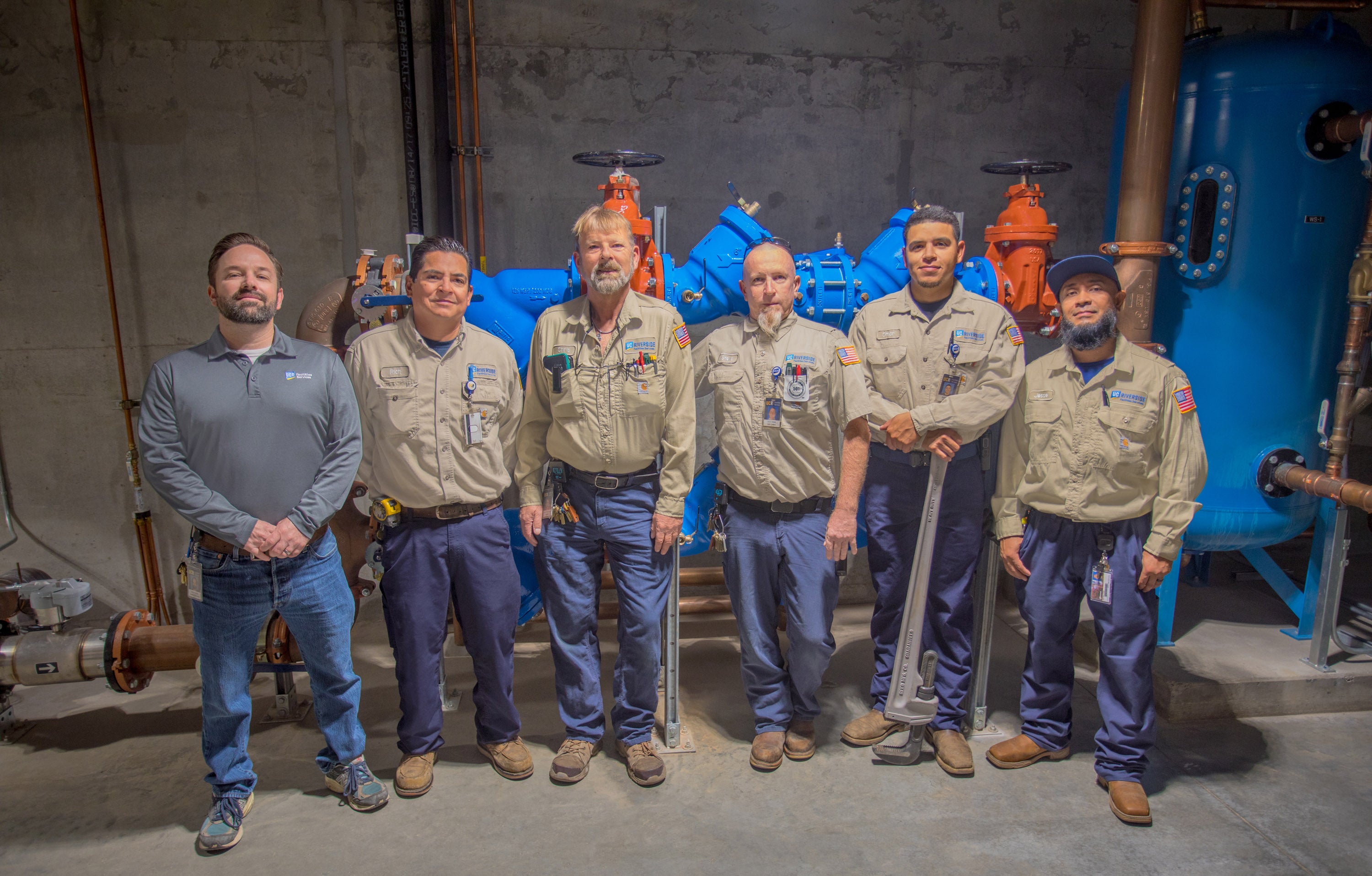 Seven workman standing in front of plumbing system in basement