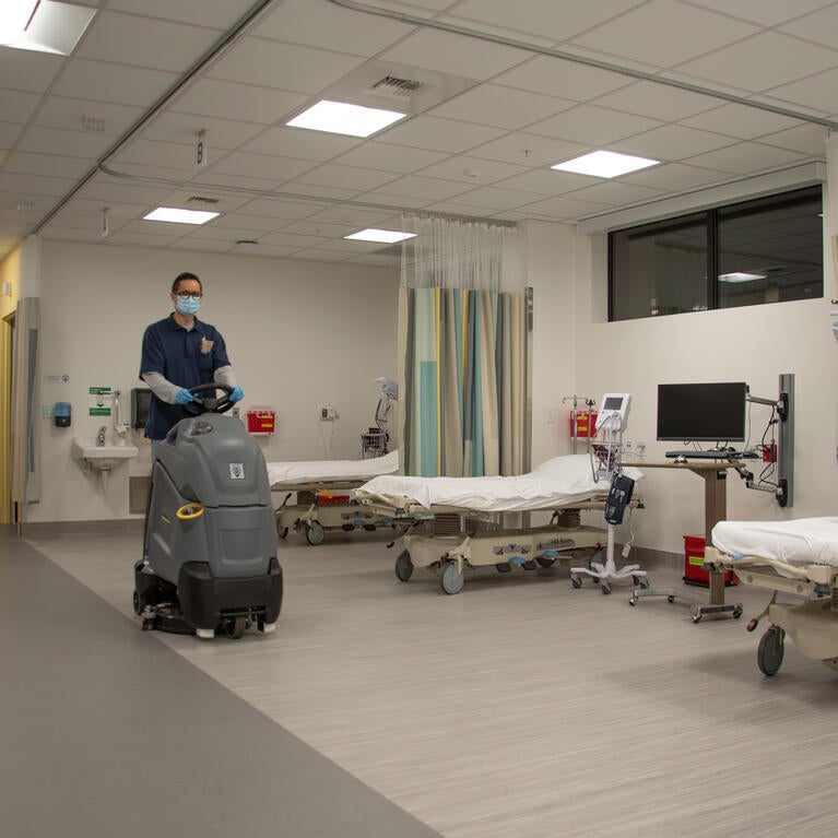 Custodian riding cleaning equipment past medical beds