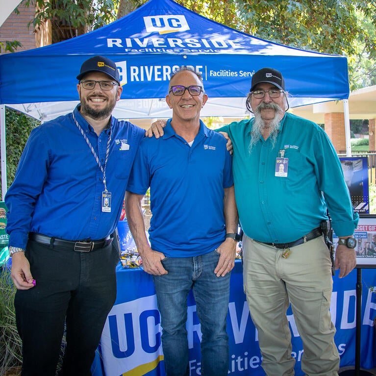 Three staff standing and smiling in front of an outdoor table