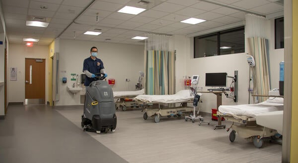 Custodian riding cleaning equipment past medical beds