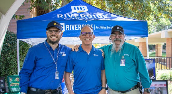 Three staff standing and smiling in front of an outdoor table
