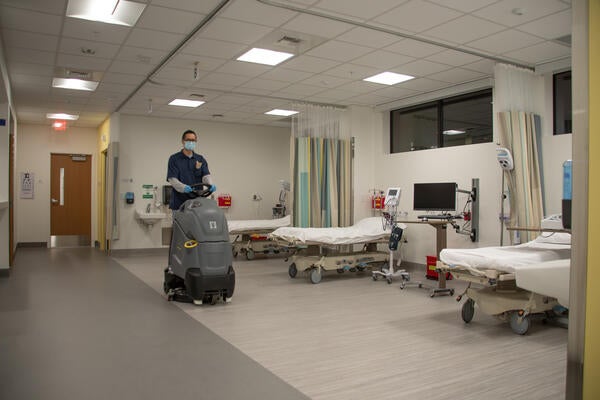 Custodian riding cleaning equipment past medical beds