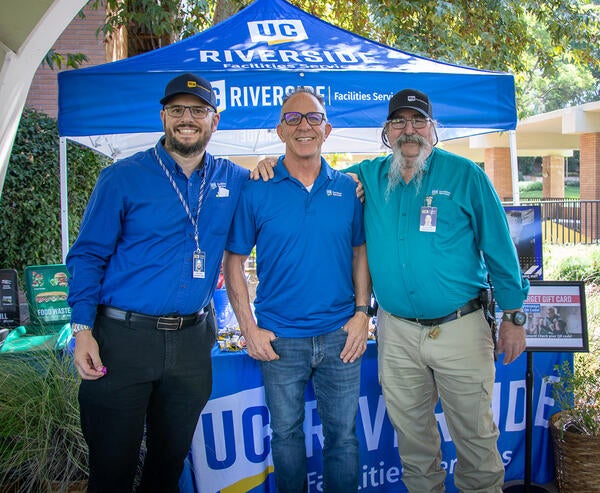 Three staff standing and smiling in front of an outdoor table