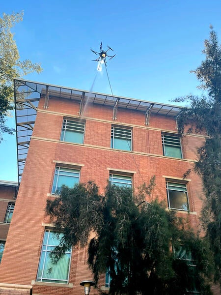 A drone power washes a window of a high-rise brick building