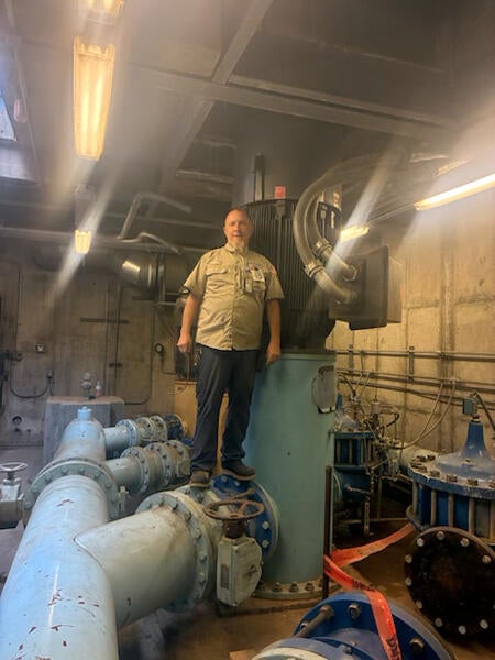  A technician stands on an enormous blue pipe inside a mechanical room