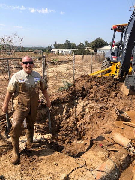 Excavation work at an agricultural site, with a worker standing beside a deep trench