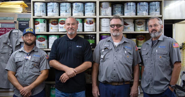 Four technicians in front of a wall of shelved paint cans