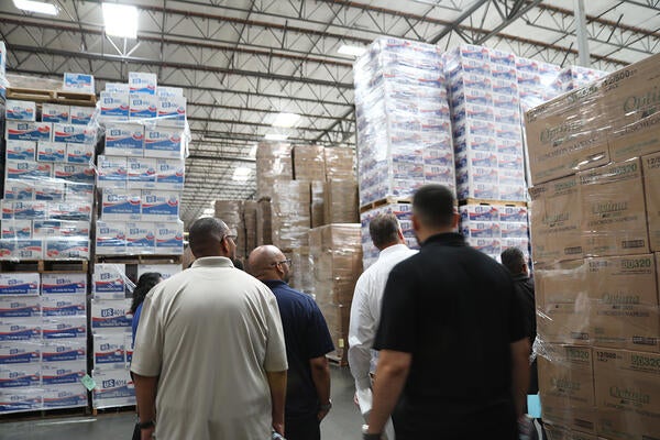 People looking at packaged paper products stacked in a warehouse